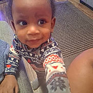 Tylan is registered to the contest to win money with this photo: carpet, child, couch, cozy, curious, cute, floor, footwear, furniture, hand, home, indoor, living_room, pajamas, patterned_clothing, person, smile, toddler, wood_floor, young_child