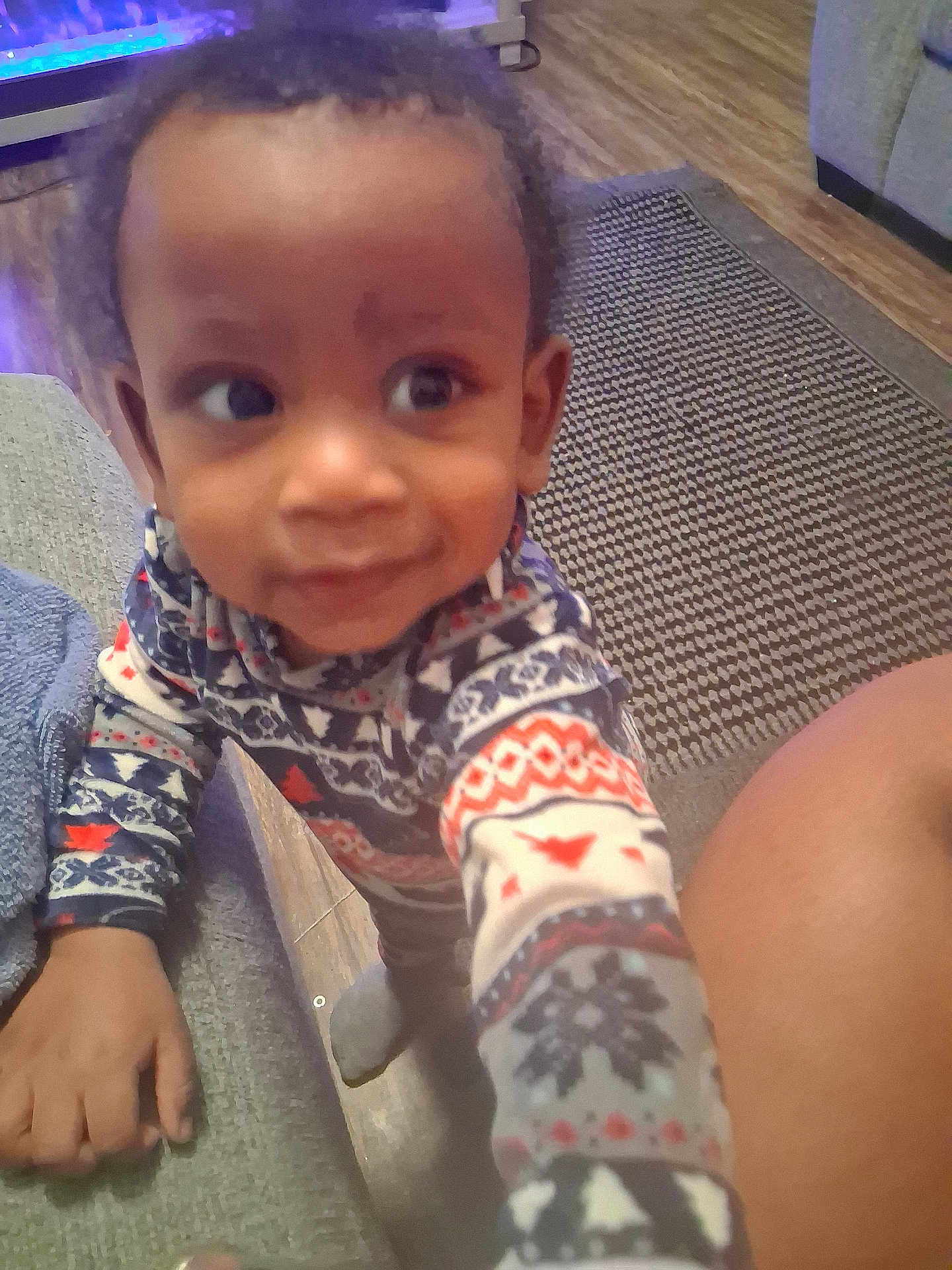 Tylan is registered to the contest to win money with this photo: carpet, child, couch, cozy, curious, cute, floor, footwear, furniture, hand, home, indoor, living_room, pajamas, patterned_clothing, person, smile, toddler, wood_floor, young_child