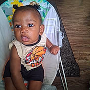 Tylan is registered to the contest to win money with this photo: baby, child, infant, sitting, baby_chair, curly_hair, pigtails, basketball_shirt, shorts, indoor, wooden_floor, rug, face, hands, clothing, furniture, person, cute, young, portrait