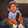 toddler, child, baby, hat, bucket_hat, blue_clothing, socks, remote_control, couch, blanket, indoor, happy, smiling, seated, furniture, person, cute, curious, young_child, home