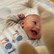 Lyvaï a rejoint le concours — aidez-le/la à gagner de superbes lots ! baby, infant, smiling, cushion, plush_toy, wooden_floor, soft_toy, happy, cute, child, indoor, clothing, person, face, lying_down, playful, cozy, infant_clothing, baby_gym, expression