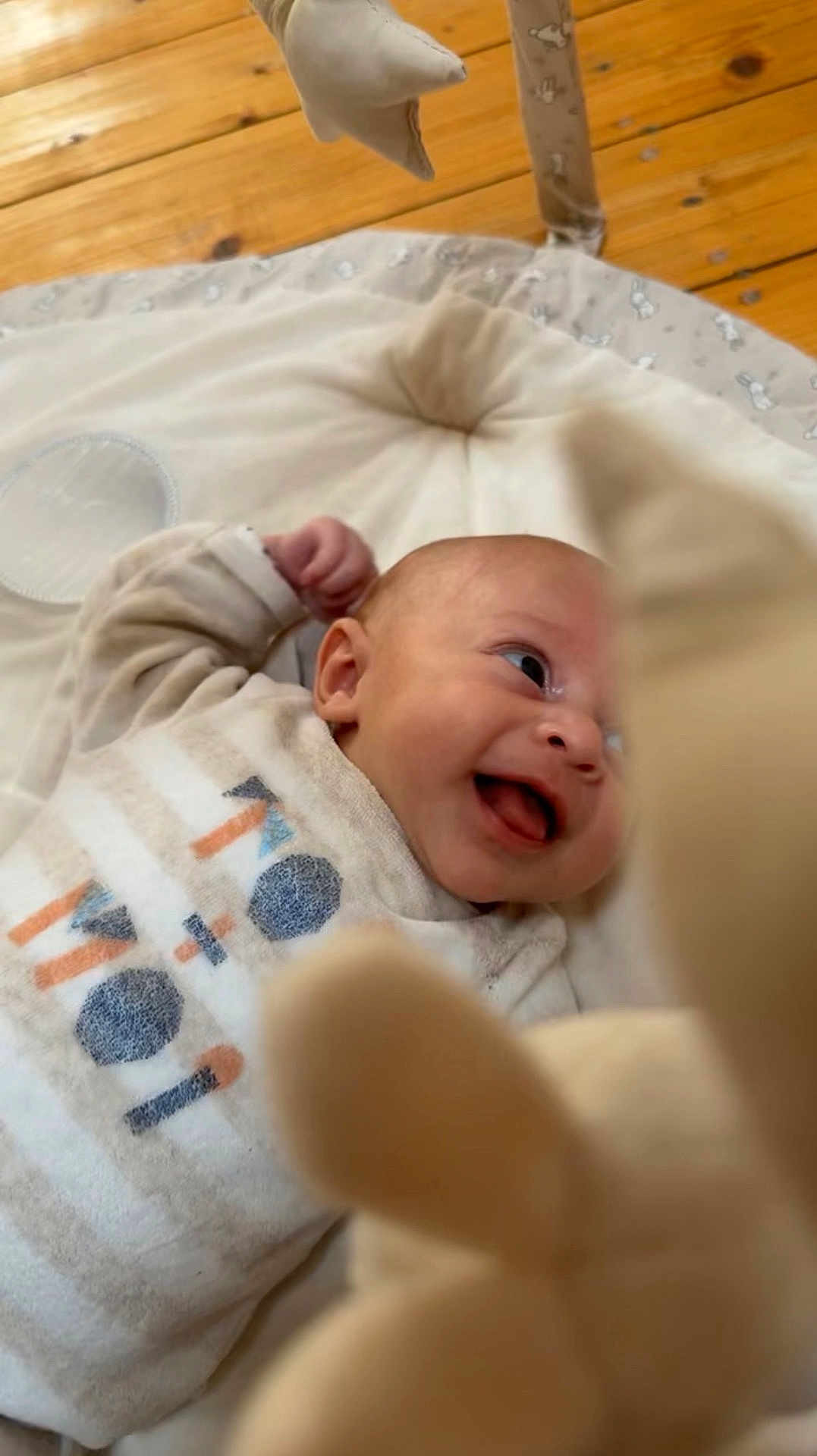 Lyvaï a rejoint le concours — aidez-le/la à gagner de superbes lots ! baby, infant, smiling, cushion, plush_toy, wooden_floor, soft_toy, happy, cute, child, indoor, clothing, person, face, lying_down, playful, cozy, infant_clothing, baby_gym, expression