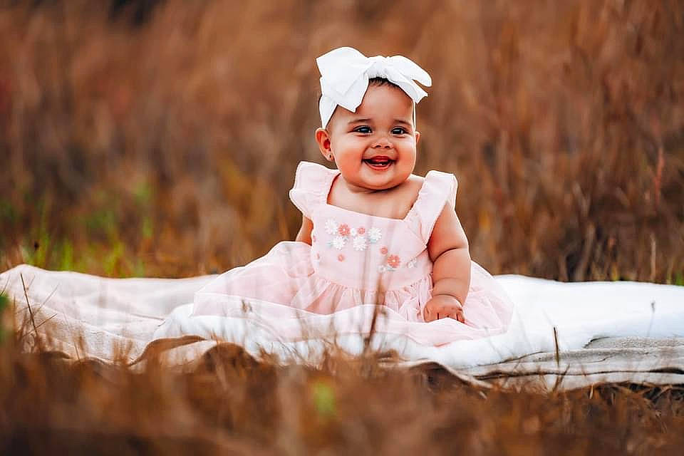 Emberly is registered to the contest to win money with this photo: baby, baby_toddler_clothing, child, dress, event, flash_photography, fun, grass, grassland, happy, headwear, joy, landscape, laugh, love, people_in_nature, person, plant, prairie, sitting