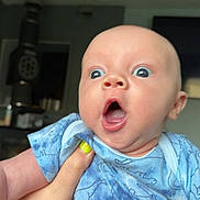 Zayden joined the competition — help win amazing prizes! baby, child, surprised, expression, hand, nail_polish, blue_clothing, onesie, dinosaur_pattern, indoor, face, person, skin, infant, cute, wide_eyes, mouth_open, holding, human, portrait