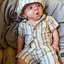 Zayden is registered to the contest to win money with this photo: baby, infant, hat, striped_clothing, shirt, shorts, bed, blanket, pillow, expression, wide_eyes, cute, child, indoors, sitting, comfortable, cozy, fabric, pattern, person