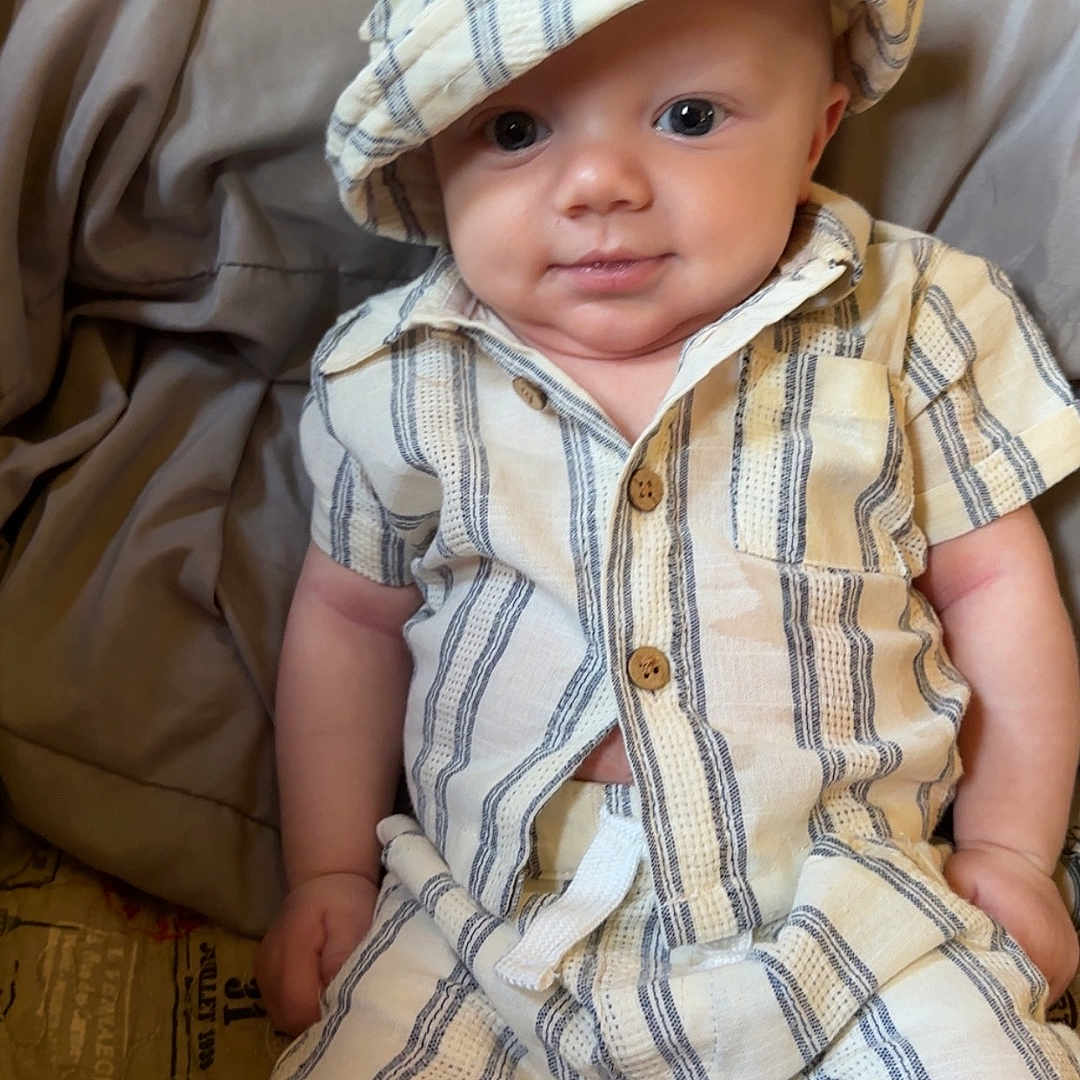 Zayden joined the competition — help win amazing prizes! baby, bed, blanket, child, comfortable, cute, eyes, face, hand, hat, indoors, infant, legs, person, relaxed, shirt, shorts, skin, smile, striped_clothing