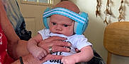 Zayden is registered to the contest to win money with this photo: baby, headphones, indoor, person, child, hands, clothing, blanket, furniture, door, dreamcatcher, wooden_chair, adult_hand, expression, foot, sitting, home, red, white, blue