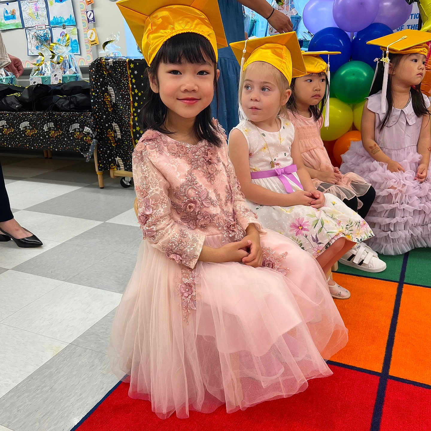 Joyee is registered to the contest to win money with this photo: artwork, balloons, carpet, celebration, child, children, classroom, dress, floor_tiles, graduation, graduation_cap, group, happy, indoor, painting, pink_dress, portrait, smiling, white_dress, yellow_cap