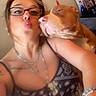 woman, dog, selfie, indoor, glasses, necklace, tattoo, bracelet, affection, pucker, shoulder, patterned_clothing, face, pet, home_decor, photography, casual, closeup, love, furniture