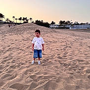 Helias a rejoint le concours — aidez-le/la à gagner de superbes lots ! child, sand, dune, sunset, outdoor, casual_clothing, tshirt, shorts, sneakers, palm_trees, sky, nature, landscape, vacation, travel, young, boy, calm, walking, daylight