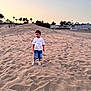 child, sand, dune, sunset, outdoor, casual_clothing, tshirt, shorts, sneakers, palm_trees, sky, nature, landscape, vacation, travel, young, boy, calm, walking, daylight