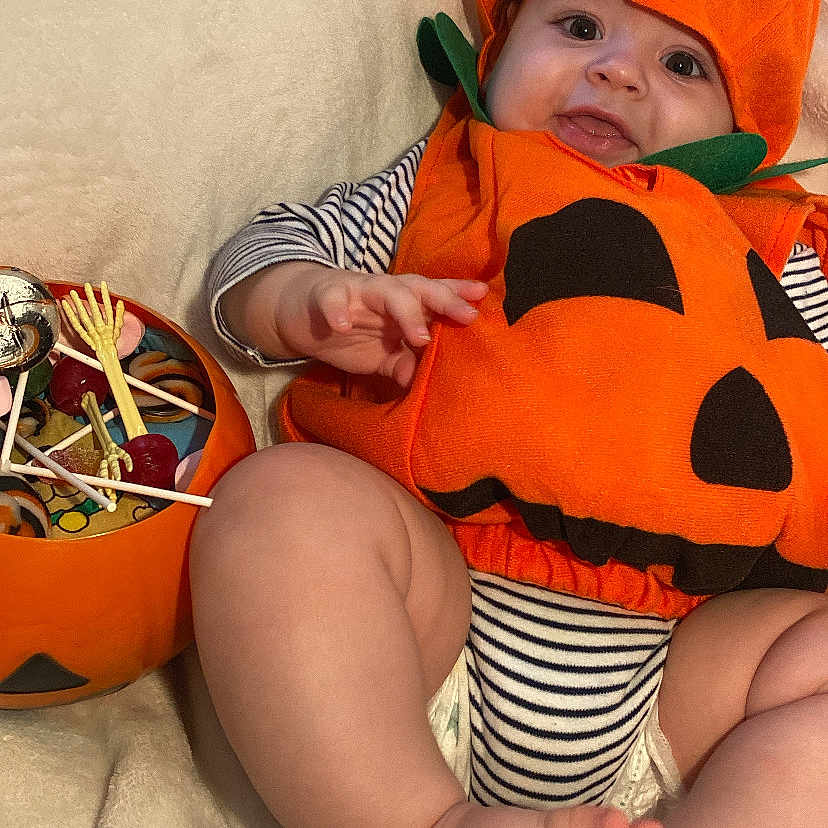 Zaïen participe au concours pour gagner de l'argent avec cette photo : baby, blanket, candy, child, costume, cute, feet, festive, halloween, hand, holiday, infant, orange, portrait, pumpkin_costume, skeleton_hand, smiling, soft_texture, striped_clothing, toy