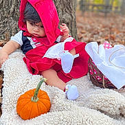 Ysabell joined the competition — help win amazing prizes! baby, child, costume, red_hood, pumpkin, blanket, tree, autumn, outdoor, nature, basket, white_cloth, fall_leaves, cute, sitting, portrait, soft_texture, curious, footwear, colorful