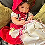 Ysabell is registered to the contest to win money with this photo: baby, child, red_hood, basket, white_fabric, pacifier, couch, green_pillow, black_leather, dress, shoes, sitting, curly_hair, indoors, exploring, cute, focused, small_hands, fabric, seated