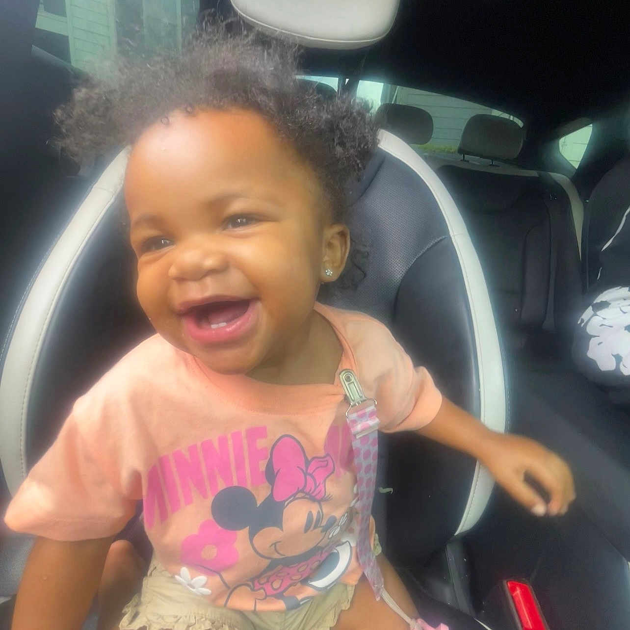 Laelani is registered to the contest to win money with this photo: toddler, child, smiling, car_seat, curly_hair, pink_shirt, minnie_mouse, pacifier, clothing, car_interior, seat, window, happy, cute, earrings, shorts, baby, person, indoor, transportation