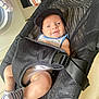 baby, baby_accessory, baby_clothing, baby_gear, baby_seat, black_cap, domestic, face, floor, happy, home, indoor, infant, laundry, mesh_carrier, person, smiling, striped_socks, washing_machine, white_onesie