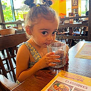 Eleysa a rejoint le concours — aidez-le/la à gagner de superbes lots ! child, girl, drinking, glass, water, restaurant, table, menu, wooden_chair, hair_buns, cute, indoor, daylight, curious, person, casual_clothing, small_person, seated, furniture, menu_card