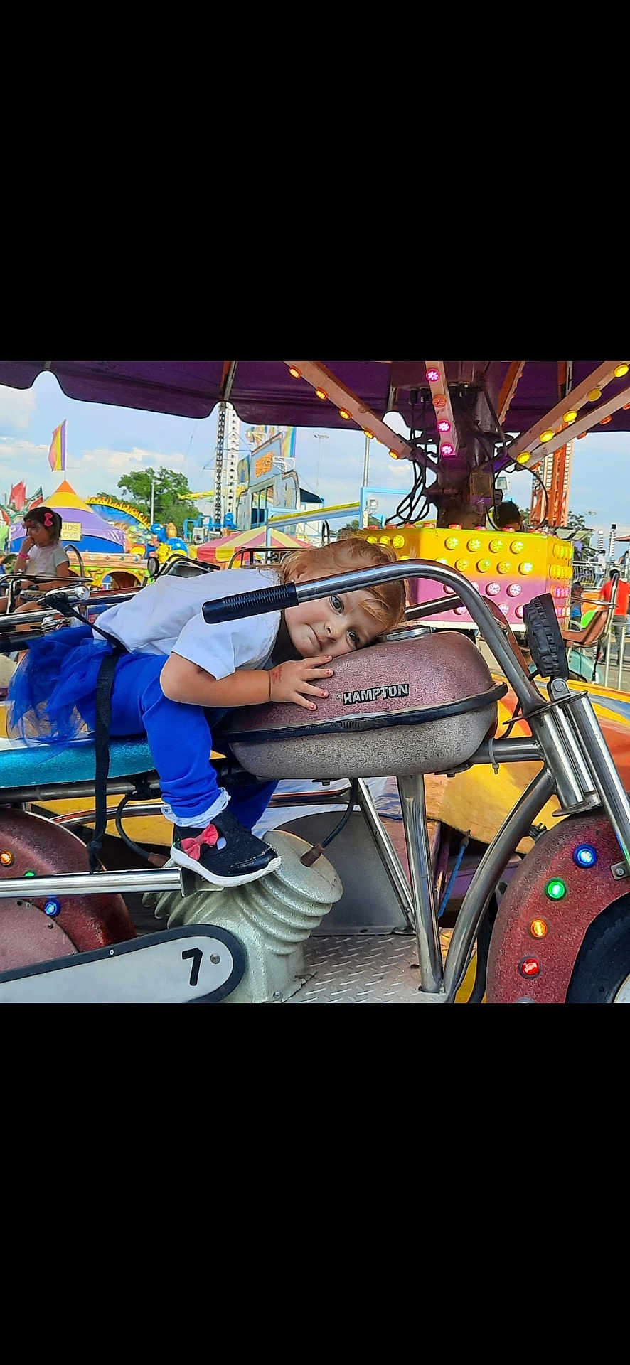 Alexa joined the competition — help win amazing prizes! child, toddler, carnival, amusement_ride, motorcycle_ride, blue_pants, white_shirt, fairground, colorful_lights, outdoor, daytime, playful, fun, seat, handlebars, young_child, casual_clothing, people, entertainment, smiling
