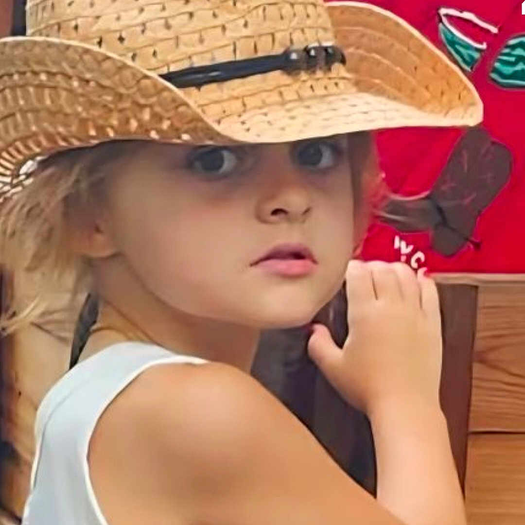 Alexa is registered to the contest to win money with this photo: child, hat, straw_hat, face, arm, blonde_hair, curious, portrait, indoor, person, butterfly, background, wood, red_background, closeup, young, expression, tank_top, skin, looking