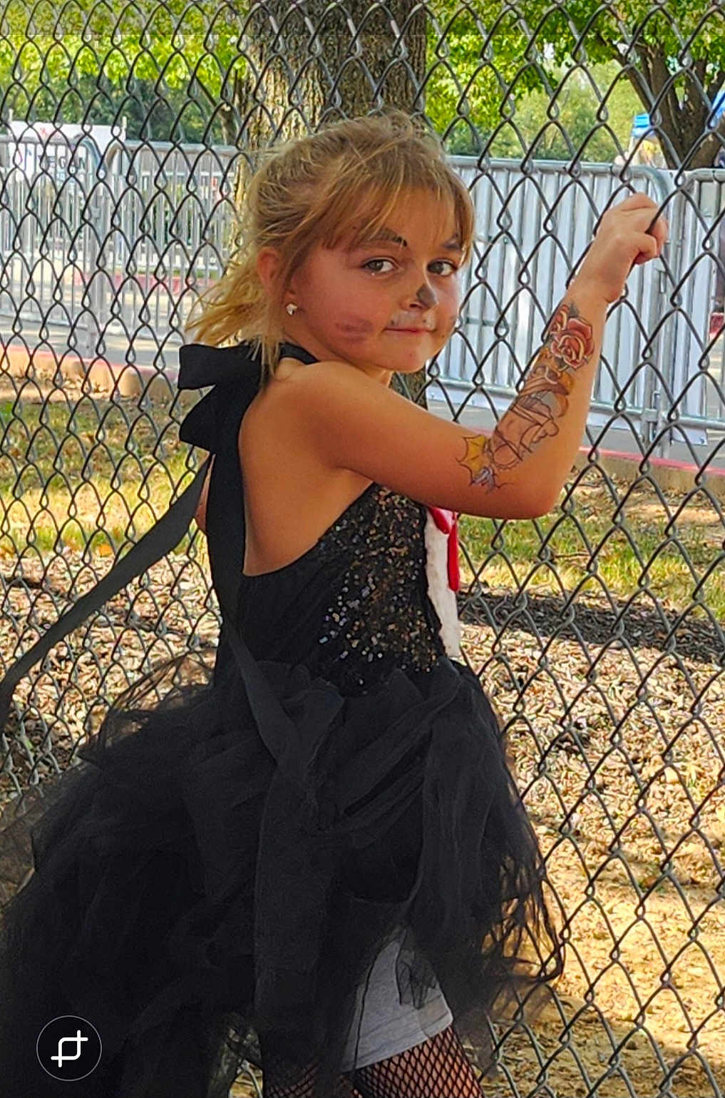 Alexa is registered to the contest to win money with this photo: child, girl, face_paint, temporary_tattoo, black_tutu, fishnet_stockings, outdoor, chain_link_fence, sunlight, trees, playful, posing, costume, summer, daylight, portrait, young, smiling, confident, casual