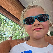 Alexa is registered to the contest to win money with this photo: child, children, portrait, selfie, sunglasses, serious_expression, name_tag, outdoor, summer, trees, patio, seating, white_shirt, blonde_hair, face, photobomb, sunlight, wooden_structure, casual, photography