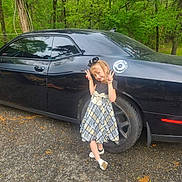 Alexa joined the competition — help win amazing prizes! child, girl, car, black_car, plaid_dress, peace_sign, outdoor, trees, smiling, posing, vehicle, wheel, road, nature, greenery, cute, happy, footwear, accessory, daylight