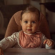 Romy participe au concours pour gagner de l'argent avec cette photo : baby, child, high_chair, bib, pink, heart_pattern, long_sleeve, indoors, face, portrait, curious, cute, young_child, person, furniture, sitting, table, expression, soft_light, hair