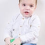 toddler, child, boy, white_shirt, blue_jeans, plush_toy, green_toy, indoor, portrait, cute, smiling, young_child, hands, sitting, casual_clothing, short_hair, light_background, studio_photo, curious_expression, face