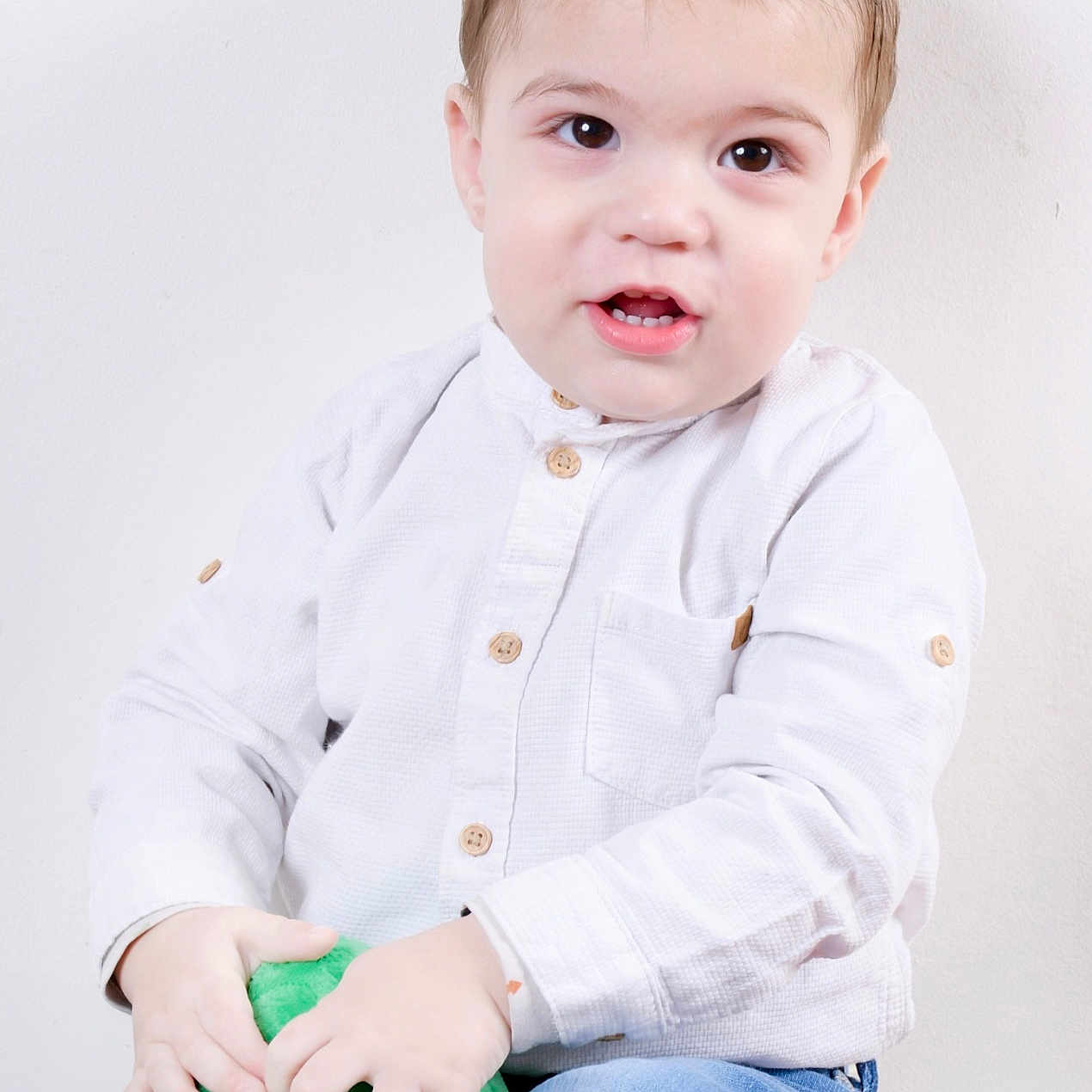 Mélio a rejoint le concours — aidez-le/la à gagner de superbes lots ! blue_jeans, boy, casual_clothing, child, curious_expression, cute, face, green_toy, hands, indoor, light_background, plush_toy, portrait, short_hair, sitting, smiling, studio_photo, toddler, white_shirt, young_child