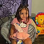 child, girl, braids, pink_shirt, hello_kitty, stuffed_animal, toy, chair, carpet, indoor, furniture, colorful_toy, lion_toy, playful, cute, smiling, hair_buns, childhood, room, relaxed