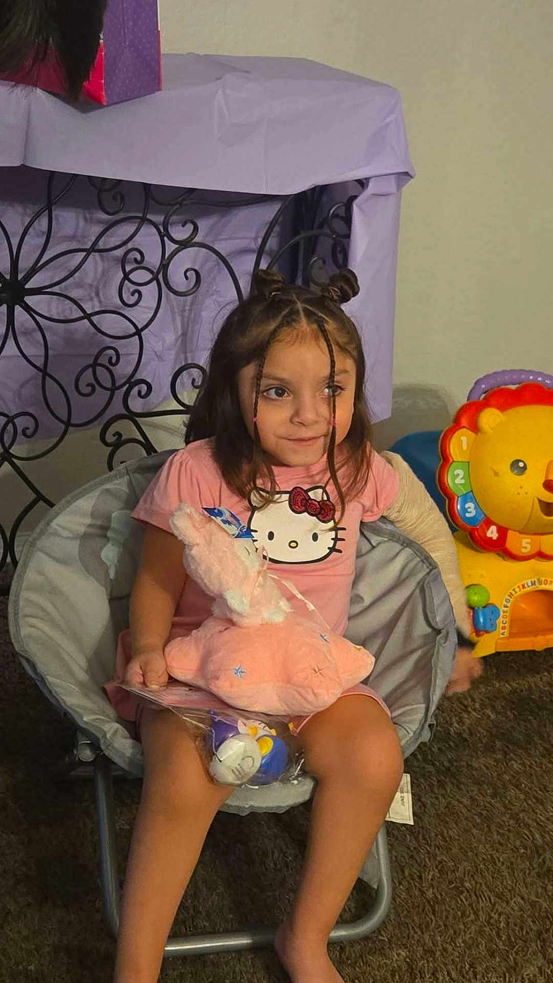Millie joined the competition — help win amazing prizes! child, girl, braids, pink_shirt, hello_kitty, stuffed_animal, toy, chair, carpet, indoor, furniture, colorful_toy, lion_toy, playful, cute, smiling, hair_buns, childhood, room, relaxed