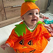 Ray-Anne is registered to the contest to win money with this photo: baby, child, pumpkin_costume, orange, green, hat, smiling, indoor, floor, wooden_furniture, cute, happy, face, sitting, costume, holiday, festive, infant, clothing, playful