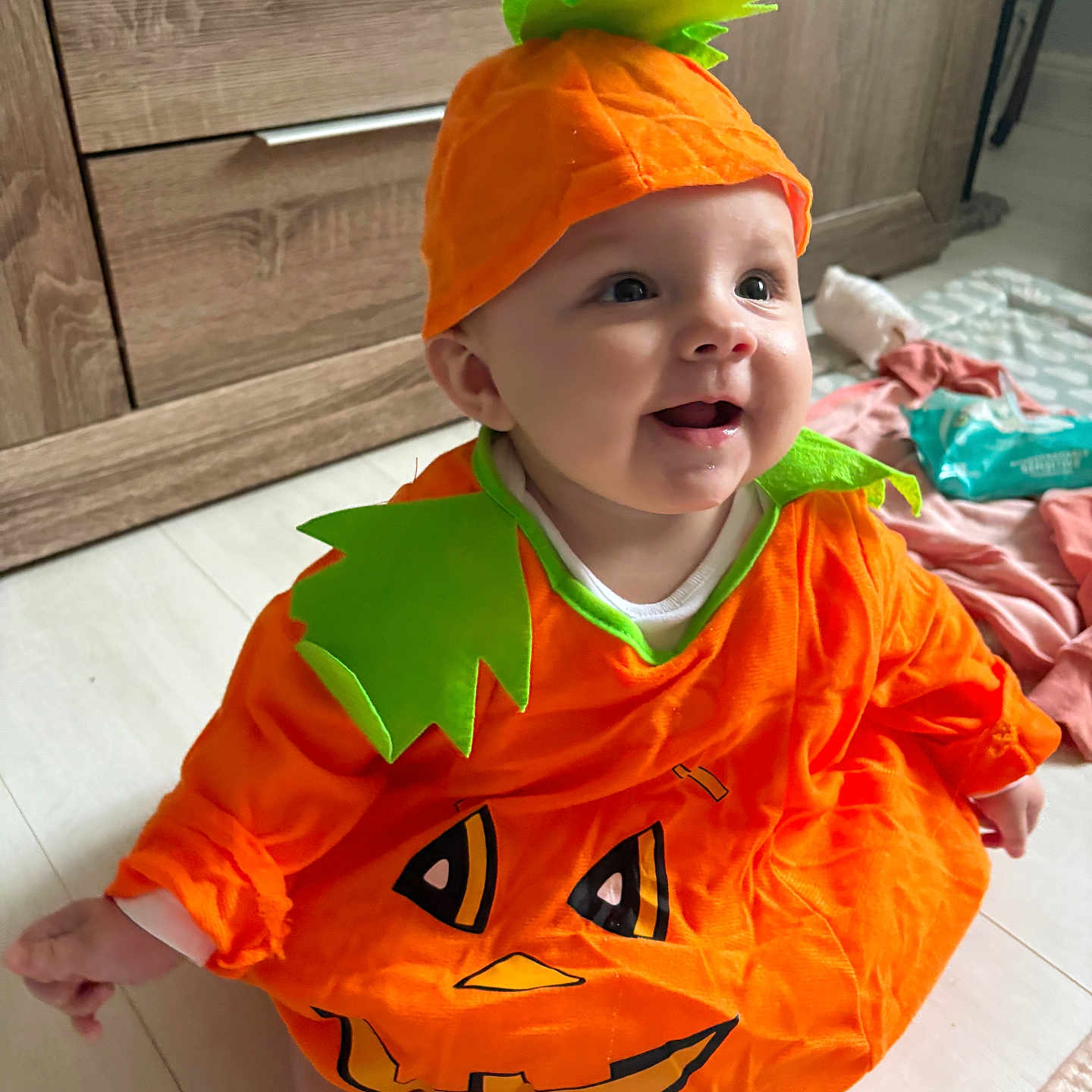 Ray-Anne is registered to the contest to win money with this photo: baby, child, clothing, costume, cute, face, festive, floor, green, happy, hat, holiday, indoor, infant, orange, playful, pumpkin_costume, sitting, smiling, wooden_furniture