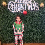 Mateo is registered to the contest to win money with this photo: child, person, holiday, christmas, festive, greenery, background, sign, ornaments, onesie, striped_clothing, slippers, standing, indoor, portrait, decor, celebration, seasonal, expressionless, floor