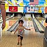 toddler, child, bowling_alley, bowling_ball, bowling_pins, tank_top, spiderman, running, smiling, wood_floor, lane, colorful, flag, american_flag, marine_flag, adult, hand, indoor, recreation, fun