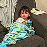 blanket, book, casual, child, comfort, couch, cozy, expression, footwear, furniture, home, indoor, person, relaxing, sippy_cup, sitting, socks, sofa, toddler, wall