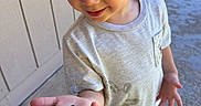 Elias is registered to the contest to win money with this photo: child, boy, bug, hand, outdoor, curious, smile, eyelashes, shorts, tshirt, shoes, pavement, wall, sunlight, person, nature, interaction, skin, casual_clothing, play