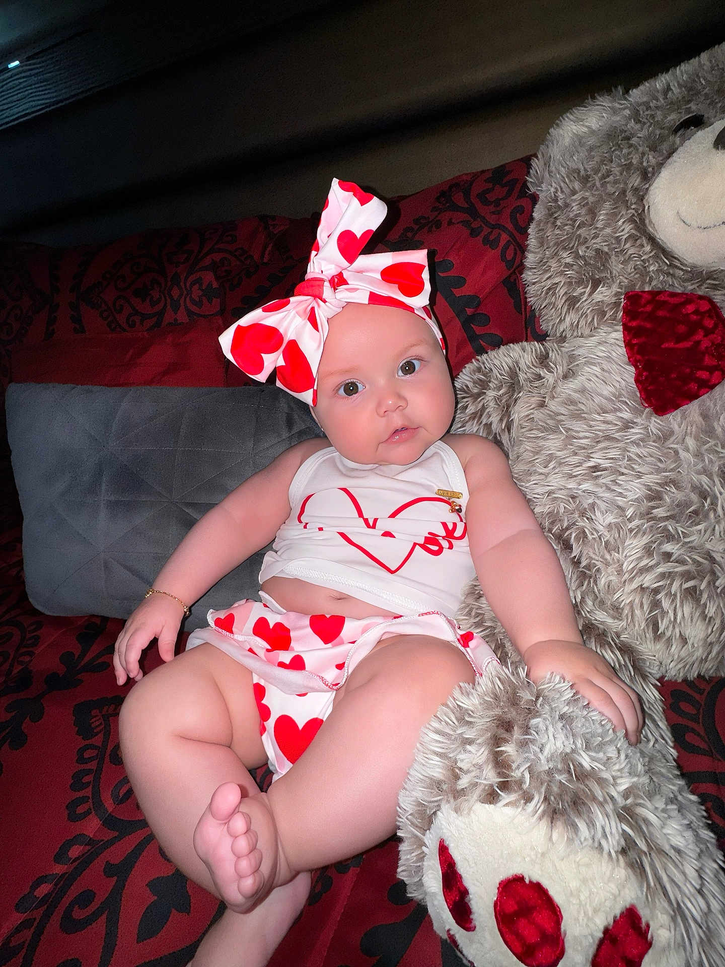 Valeria is registered to the contest to win money with this photo: baby, infant, heart_pattern, headband, teddy_bear, plush_toy, couch, pillow, red, white, skin, face, foot, hand, clothing, smile, indoor, cute, child, portrait