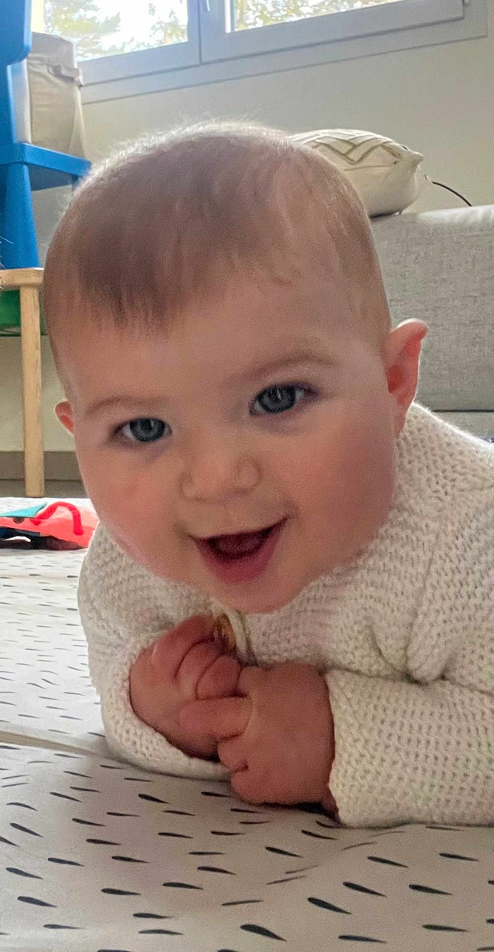 Alma participe au concours pour gagner de l'argent avec cette photo : baby, smiling, infant, hands, face, eyes, knit_sweater, floor_mat, indoor, window, chair, cushion, home, child, cute, person, portrait, cozy, happy, toddler