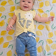 Aurora joined the competition — help win amazing prizes! baby, smiling, infant, headband, yellow_shirt, blue_pants, floral_pattern, blanket, lemon_pattern, toy, carpet, cute, happy, child, toddler, lying_down, indoor, clothing, person, accessory