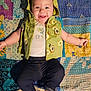 Aurora is registered to the contest to win money with this photo: baby, child, smiling, happy, hooded_vest, green_clothing, pants, barefoot, patchwork_quilt, colorful, patterned, infant, lying_down, cute, cheerful, portrait, indoor, textile, fabric, playful