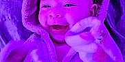 Leilani is registered to the contest to win money with this photo: apparel, baby, blanket, child, cozy, cute, face, happy, hooded_clothing, indoor, infant, mittens, person, playful, portrait, purple_light, smiling, soft_texture, warm, young