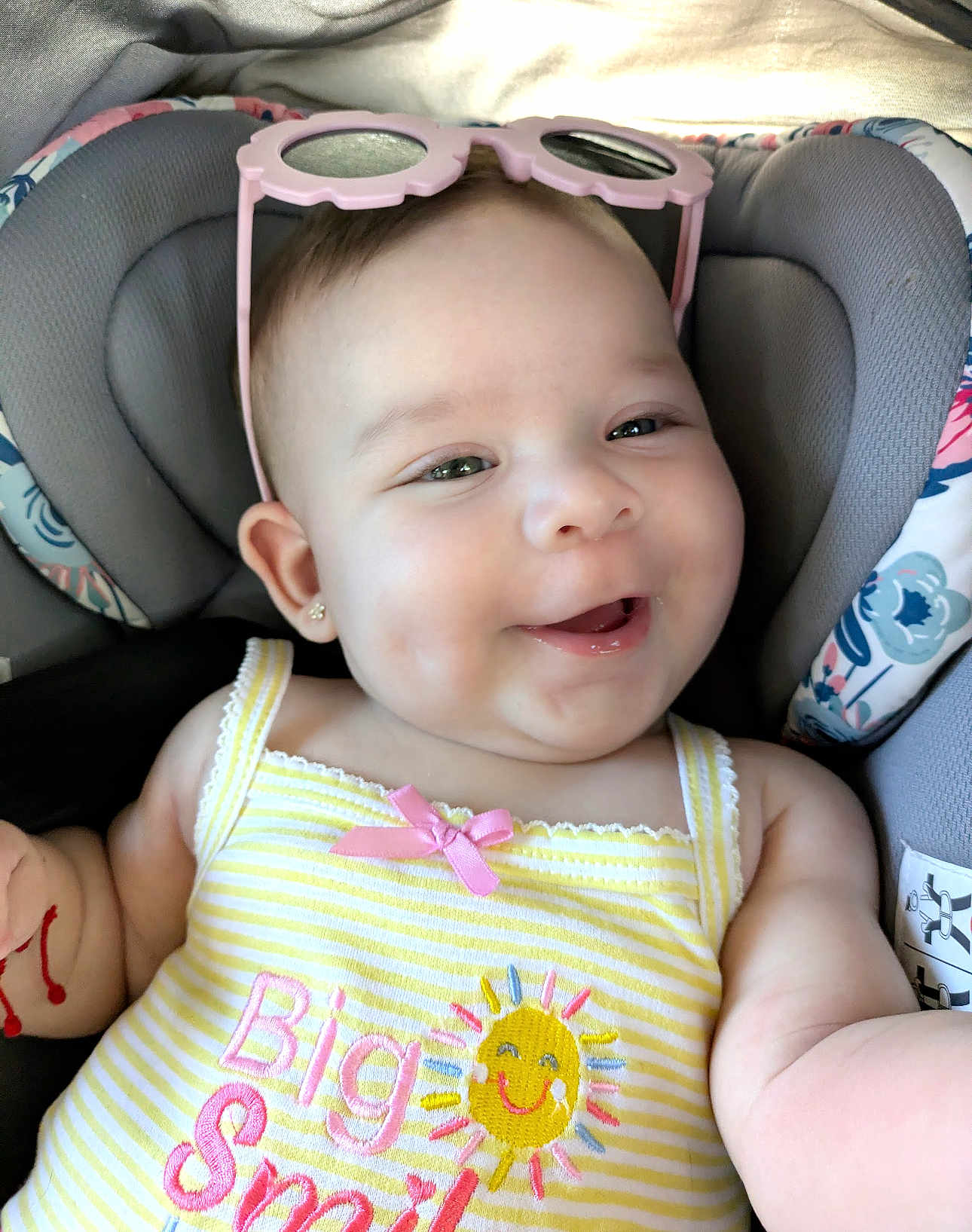 Leilani joined the competition — help win amazing prizes! baby, smiling, sunglasses, car_seat, yellow_dress, sun_embroidery, pink_bow, happy, child, cute, indoor, portrait, infant, clothing, seatbelt, fun, cheerful, accessory, headwear, closeup