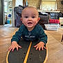 Swann participe au concours pour gagner de l'argent avec cette photo : baby, basket, casual_clothing, child, curious, expression, face, floor, furniture, hands, head, home_interior, indoor, living_room, person, playful, skateboard, smiling, sofa, wooden_floor