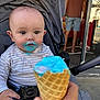 baby, blue_ice_cream, blurred_background, casual_clothing, child, cone, daylight, expression, face, food, hand, ice_cream, messy, mouth, outdoor, person, stroller, summer, sweet, toddler