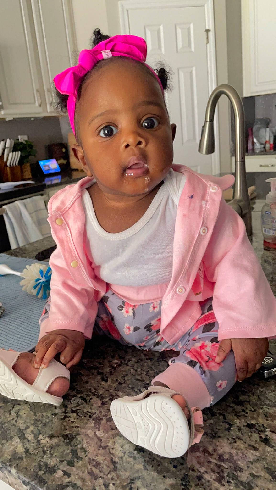 Melodie is registered to the contest to win money with this photo: baby, baby_toddler_clothing, cheek, child, dress, eyelash, flooring, fun, happy, human_body, kitchen_appliance, magenta, person, pink, purple, sitting, skin, sleeve, standing, t_shirt