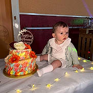Nathanaël a rejoint le concours — aidez-le/la à gagner de superbes lots ! baby, child, cake, table, flowers, string_lights, indoors, celebration, baptism, white_clothing, cardigan, decorations, flower_cake, light, face, sitting, cute, party, event, infant