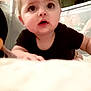 baby, infant, child, crawling, black_shirt, wide_eyes, indoor, soft_surface, curious, tousled_hair, person, young_child, face, hands, expression, closeup, home, playpen, background, light