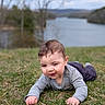 baby, child, grass, outdoor, nature, lake, water, trees, sky, cloudy, portrait, smiling, happy, casual_clothing, infant, crawling, greenery, young, playful, daytime