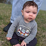 Jacob Enmanuel joined the competition — help win amazing prizes! toddler, child, grass, barefoot, sweater, cartoon_print, pants, adult, legs, outdoor, nature, casual_clothing, expression, skin, foot, hand, person, daylight, young_child, sitting